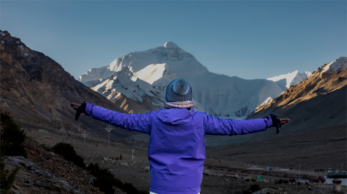A person standing with arms outstretched in front of Mount Everest