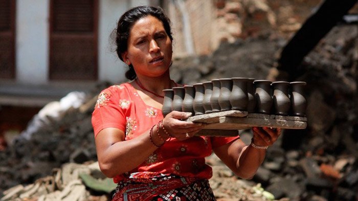 A Nepalese pottery maker is carrying newly-made pottery.