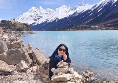 Traveler photo: A guest smiles by Ranwu Lake in Nyingchi, with snow-capped peaks behind—a relaxed and beautiful scene.  (April 2026)