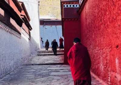 Traveler photo:  In a narrow Lhasa lane, a red-robed monk walks swiftly, as if rushing to his next practice. (April 2026)