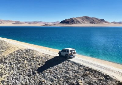 Traveler photo: A vehicle follows the lakeside road through Tibet's vast open landscape. (August 2026)