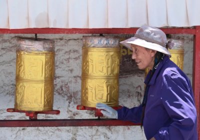 Traveler photo: A local stands before a prayer wheel, gently spinning its bronze body while murmuring a mantra. (August 2026)