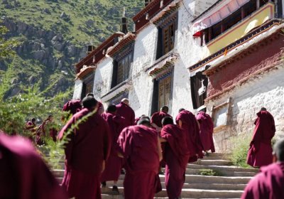 Traveler photo: Tibetan monks in deep red robes make their way toward the debate yard. (August 2025)