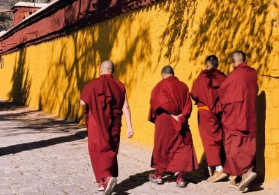 Traveler photo: Beside the yellow courtyard walls of a monastery in Lhasa, Tibet, three red-robed monks walk side by side through ancient alleys. (December 2025)
