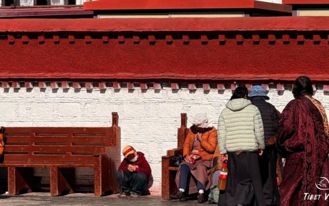 Traveler photo: At corners of traditional architecture on Barkhor Street in Lhasa, a red-robed monk uses brief leisure moments for meditation beside red-and-white walls. (January 2026)