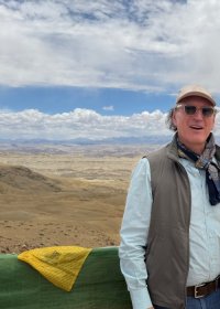 Traveler photo: A guest stands still on a hillside in Tibet, gazing at distant snow mountains and river valleys with calm focus. (July 2026)