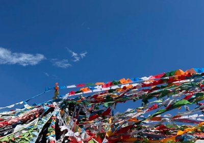Traveler photo: Wind stirs the five-colored prayer flags—blue, white, red, green, yellow—vivid under the plateau sun. (July 2026)