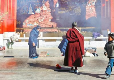 Traveler photo: At Thousand-Buddha Cliff near Lhasa, a red-robed monk prays devoutly before ancient rock-carved Buddhas. (March 2026)