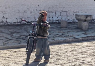 Traveler photo: A Tibetan kid stands beside his bike, gazing at the quiet, peaceful landscape of the Lhasa street. (March 2026)	