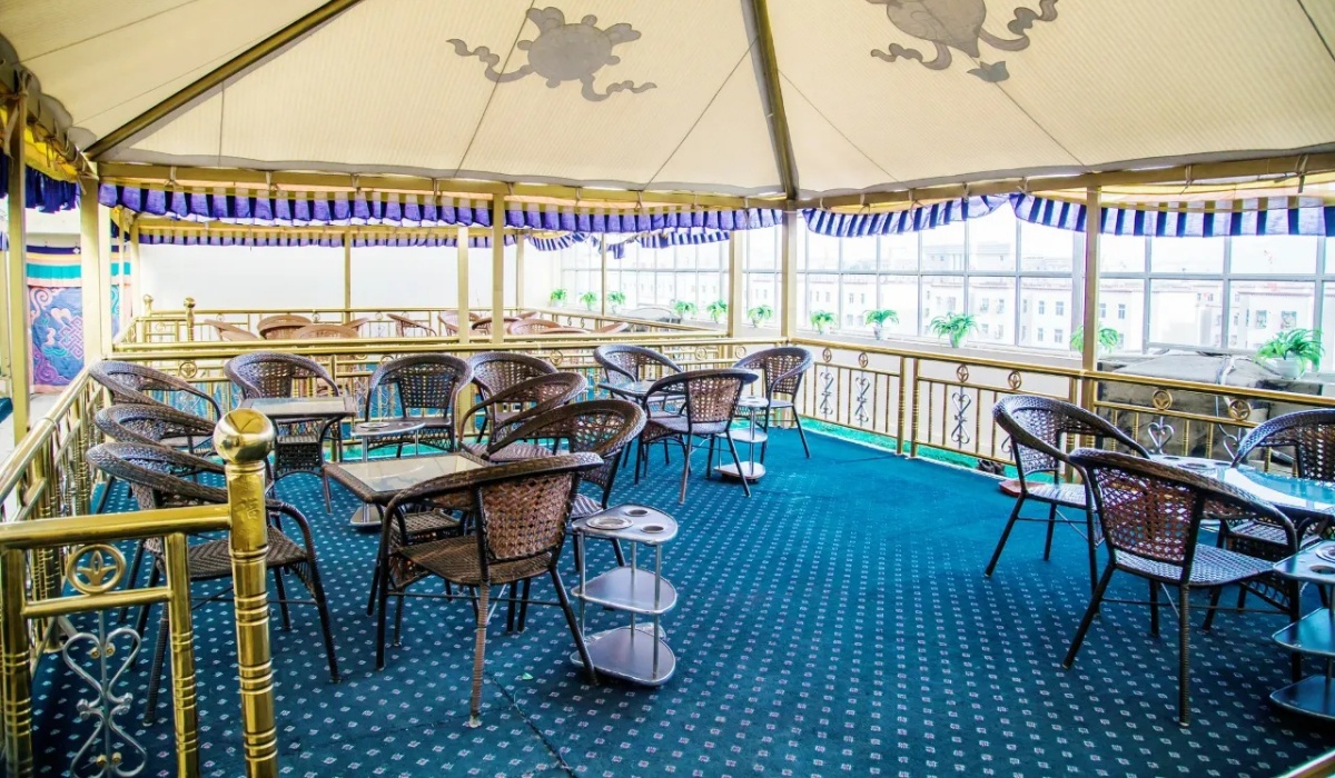 Rooftop sunroom tea lounge with rattan chairs at Gesar Hotel