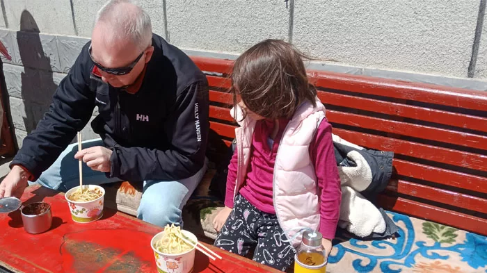 A father showing his daughter how to eat Tibetan noodles