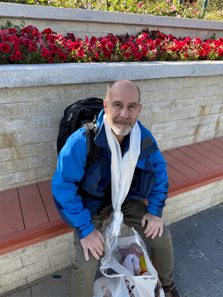 friend Colin sitting by flowers in Lhasa