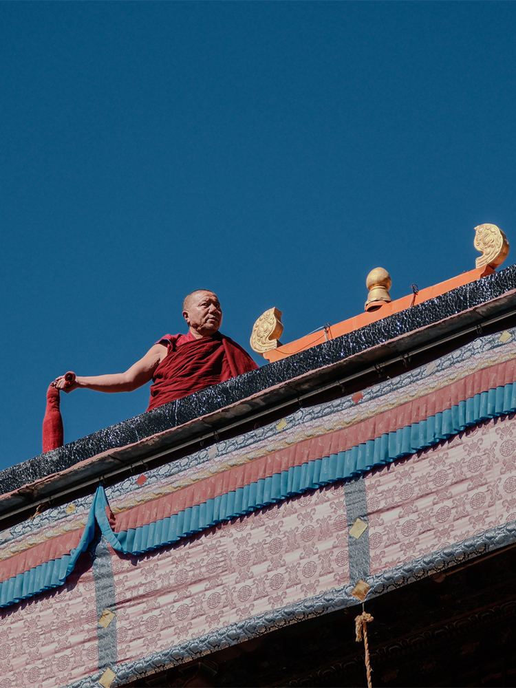 Tibetan monk cleaning monastery rooftop under clear sky