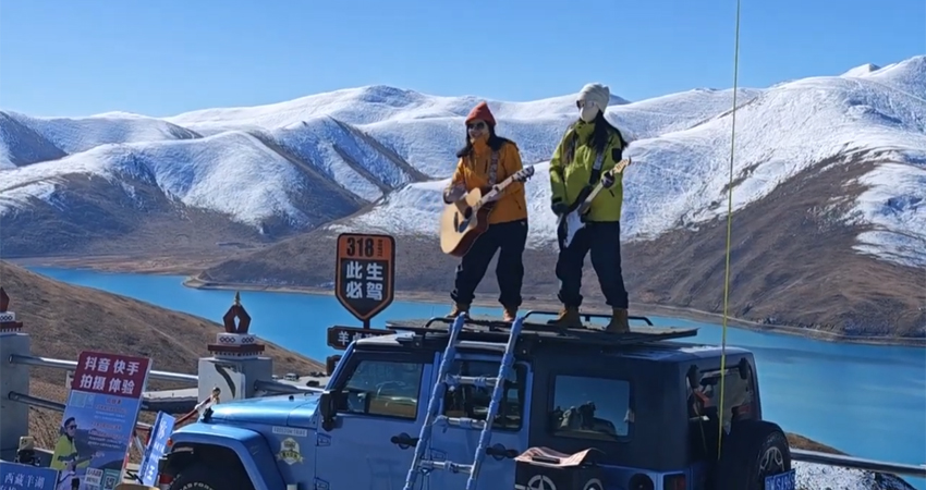Playing guitar on SUV roof by turquoise Yamdrok Lake in Tibet